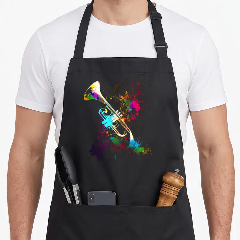 Tablier de cuisine noir avec une trompette stylisée aux couleurs vives et des éclats d'encre abstraits sur le devant.