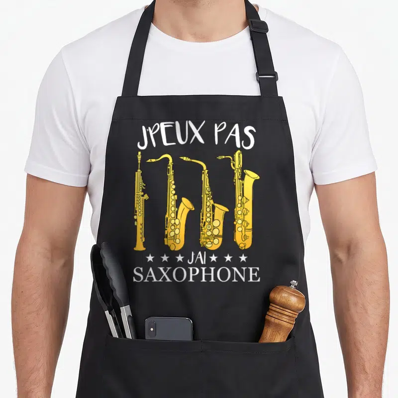 Tablier de cuisine noir avec inscription Jpeux pas j'ai saxophone et quatre saxophones jaunes alignés verticalement.
