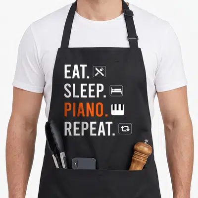 Tablier de cuisine noir avec texte blanc et orange Eat Sleep Piano Repeat accompagné d'icônes minimalistes.