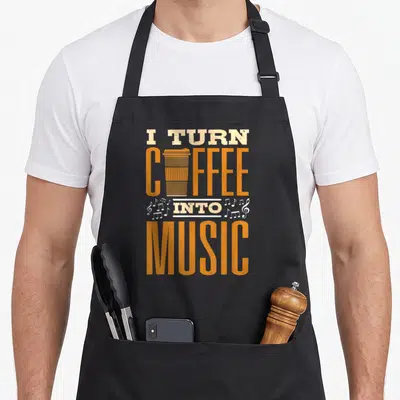 Tablier de cuisine noir avec inscription I Turn Coffee Into Music et illustration de gobelet orange et notes de musique blanches.