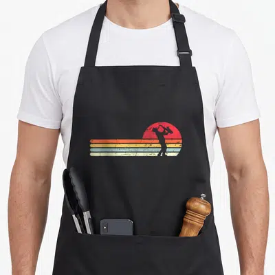 Tablier de cuisine noir avec silhouette de saxophonie devant un soleil couchant aux bandes orange, jaune et bleu pastel.