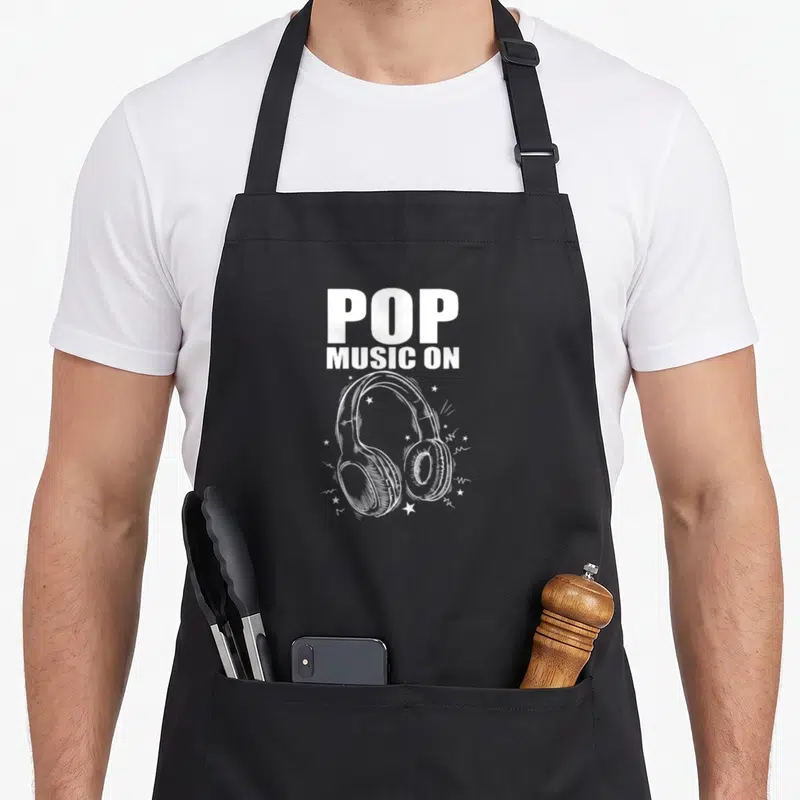 Tablier de cuisine noir avec illustration blanche de casque audio et texte Pop Music On entouré d'étoiles.
