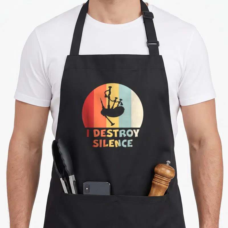 Tablier de cuisine noir avec illustration vintage d'une cornemuse et le texte I DESTROY SILENCE en lettres colorées.