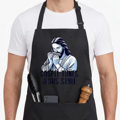 Tablier de cuisine noir avec illustration de Jésus jouant de l'harmonica et le texte Gospel Tunes Jesus Style imprimé en bas.