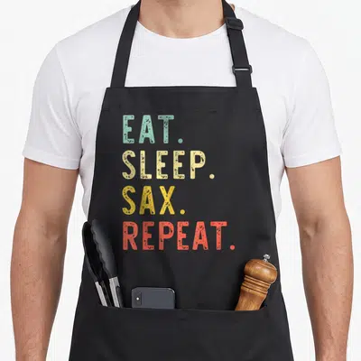 Tablier de cuisine noir avec le texte Eat Sleep Sax Repeat en lettres colorées style vintage.