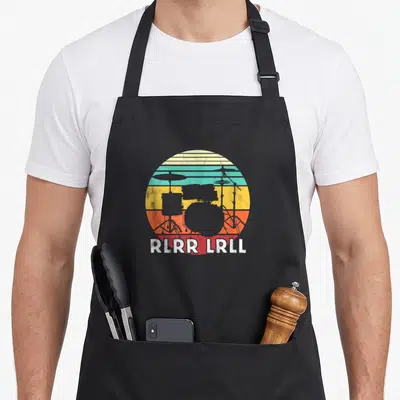 Tablier de cuisine noir avec illustration rétro d'une batterie et texte Rlrr Lrll en blanc.