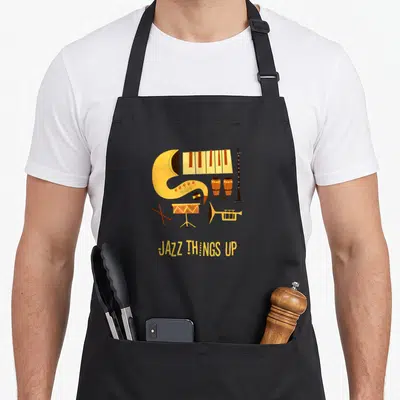 Tablier de cuisine noir avec illustration colorée de saxophone, piano et texte Jazz Things Up en jaune.