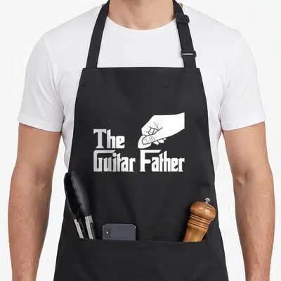 Tablier de cuisine noir avec illustration blanche d'une main tenant une pince et le texte The Guitar Father