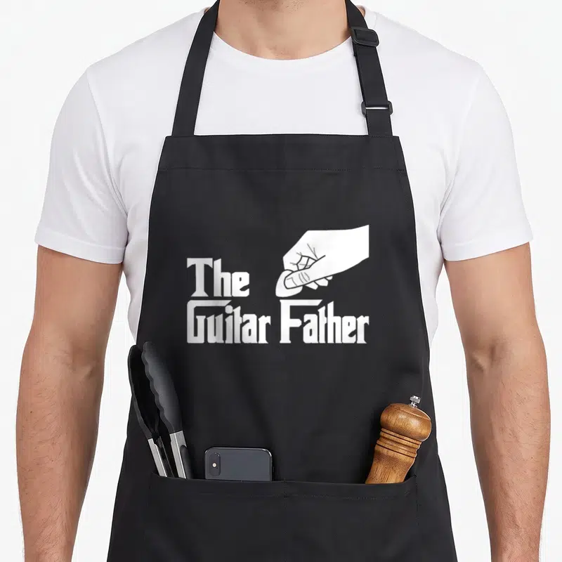 Tablier de cuisine noir avec illustration blanche d'une main tenant une pince et le texte The Guitar Father