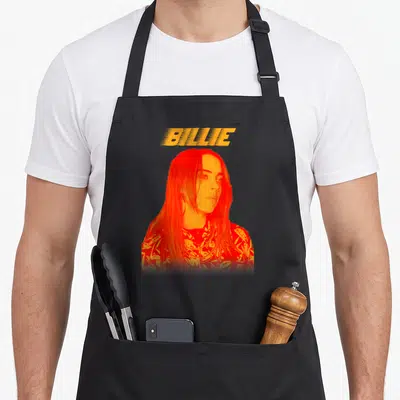 Tablier de cuisine noir avec portrait orange vif et texte BILLIE en haut.