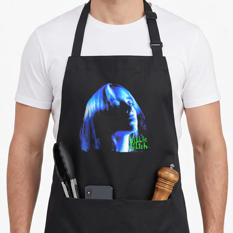 Tablier de cuisine noir avec portrait bleu stylisé et texte billie eilish en vert lime sur le côté droit.