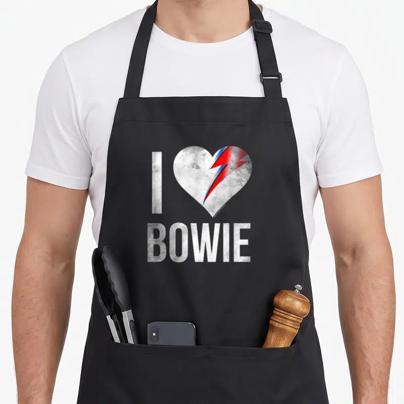 Tablier de cuisine noir avec un cœur blanc cassé traversé par un éclair rouge et bleu surmontant le mot BOWIE en lettres capitales blanches.