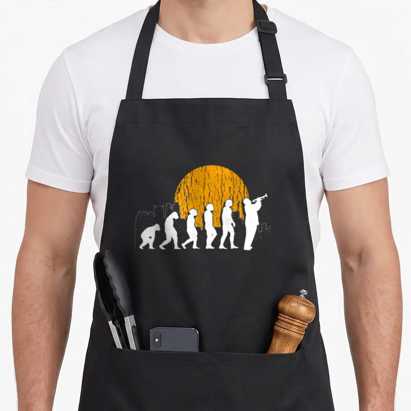Tablier de cuisine noir avec silhouette évolutive se transformant en trompettiste sous un soleil orange et une ville.