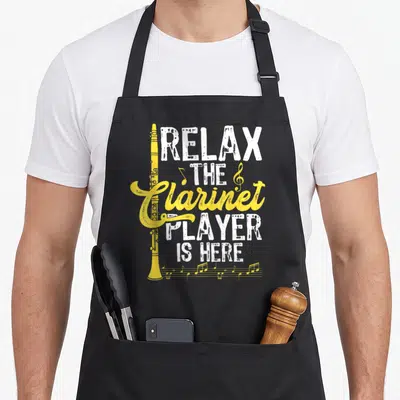 Tablier de cuisine noir avec une clarinette jaune et le texte Relax The Clarinet Player Is Here imprimé en blanc et jaune.