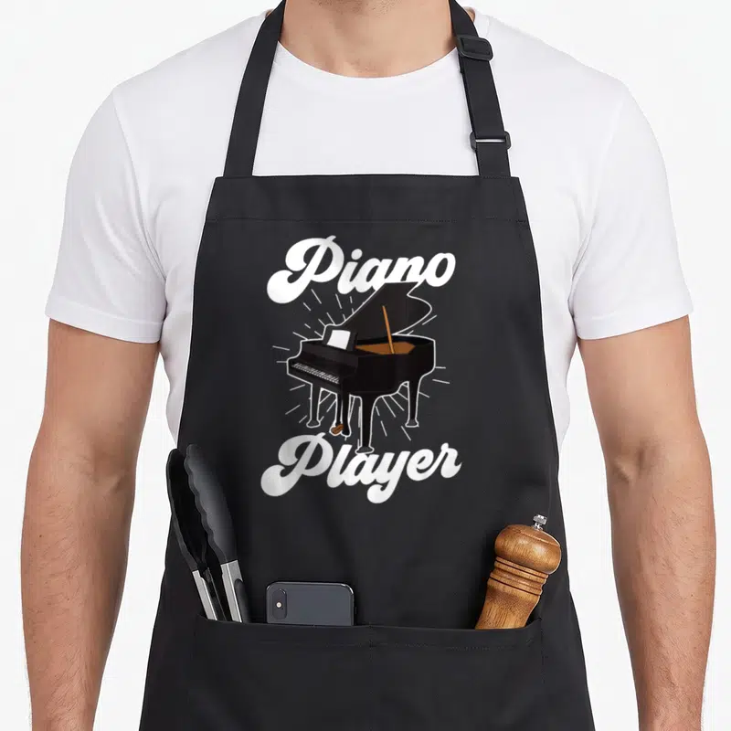 Tablier de cuisine noir avec illustration de piano à queue et texte blanc Piano Player en typographie cursive vintage.