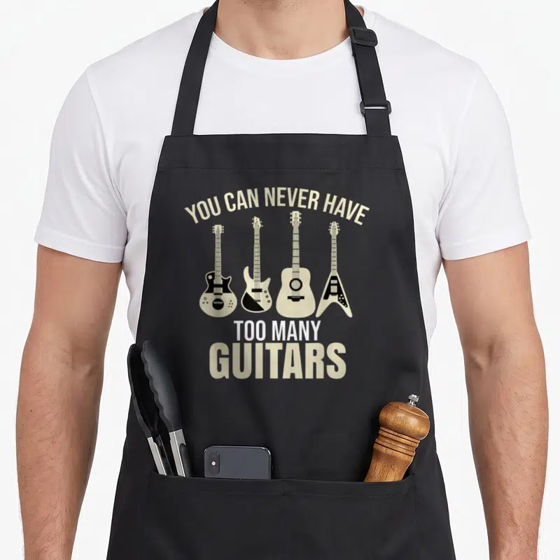 Tablier de cuisine noir avec quatre guitares et l'inscription You Can Never Have Too Many Guitars en beige et blanc.