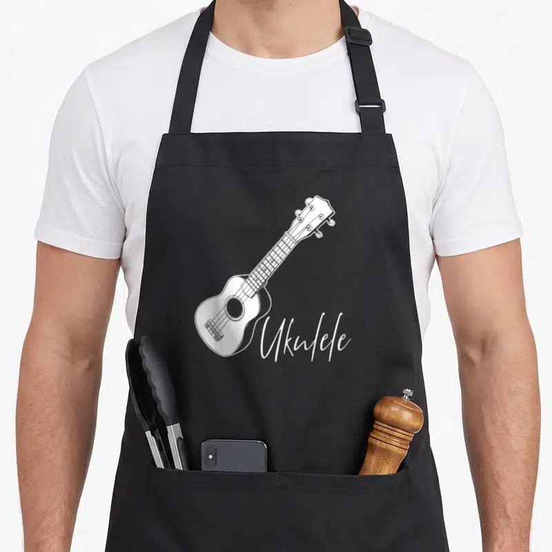 Tablier de cuisine noir avec illustration blanche d'un ukulélé et du mot Ukulele en calligraphie.