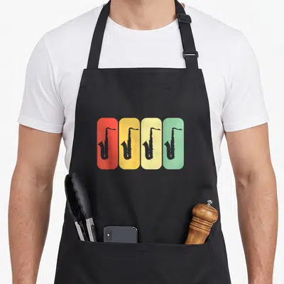 Tablier de cuisine noir avec quatre silhouettes de saxophones sur fonds rectangulaires colorés rouge, jaune, crème et vert pastel.