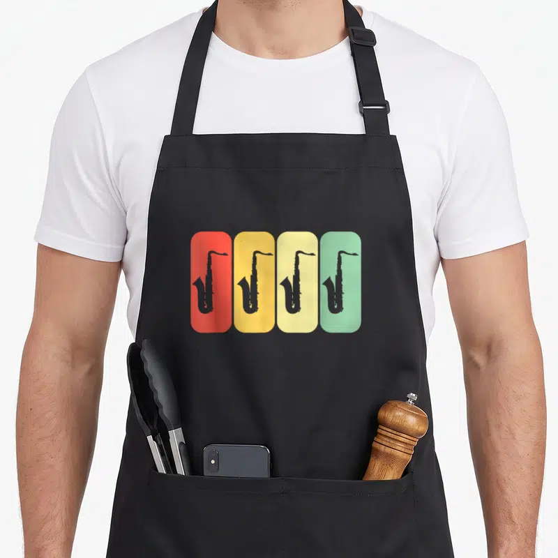 Tablier de cuisine noir avec quatre silhouettes de saxophones sur fonds rectangulaires colorés rouge, jaune, crème et vert pastel.