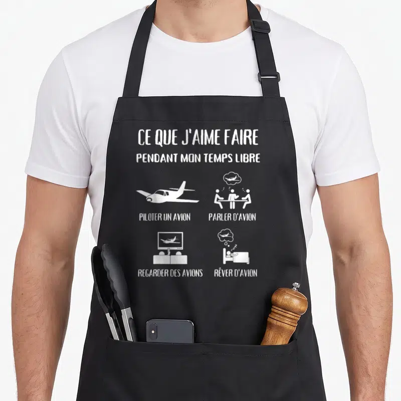 Tablier de cuisine noir avec illustrations blanches représentant un avion, des discussions et des rêves liés à l'aviation.
