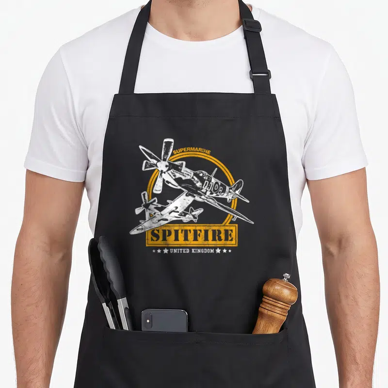 Tablier de cuisine noir avec illustration vintage d'un avion Supermarine Spitfire blanc et texte orange United Kingdom.