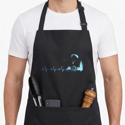 Tablier de cuisine noir avec un parapente bleu, une montagne et un arbre stylisés sur fond uni.