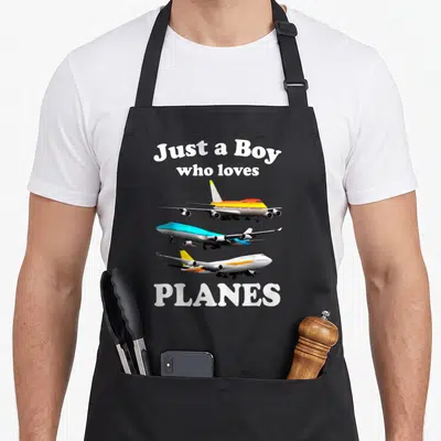 Tablier de cuisine noir avec trois avions colorés et le texte Just a Boy who loves Planes imprimé en blanc.