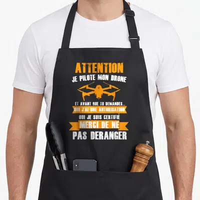 Tablier de cuisine noir avec illustration drone orange et texte blanc Attention Je Pilote Mon Drone Merci De Ne Pas Deranger.