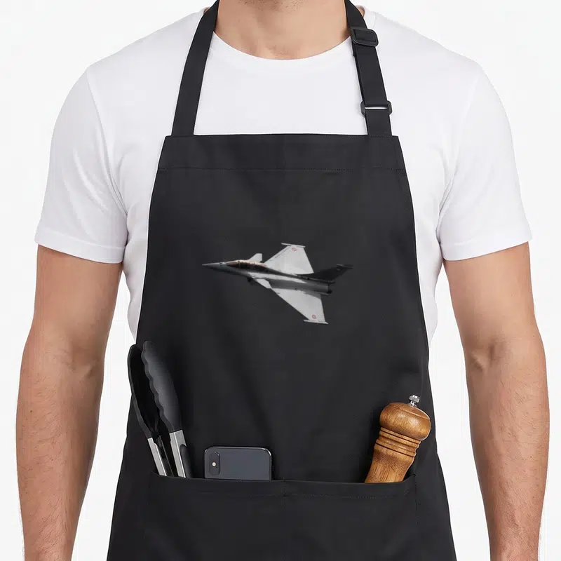 Tablier de cuisine noir avec un avion de chasse Rafale Airplane gris en plein vol sur fond uni.