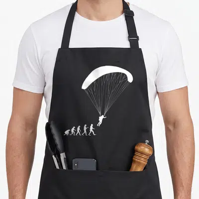 Tablier de cuisine noir avec silhouette blanche représentant l'évolution humaine se terminant par un parapentiste en vol.