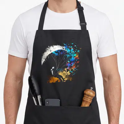 Tablier de cuisine noir avec une illustration de parapentiste aux couleurs vives et style éclaboussure de peinture.