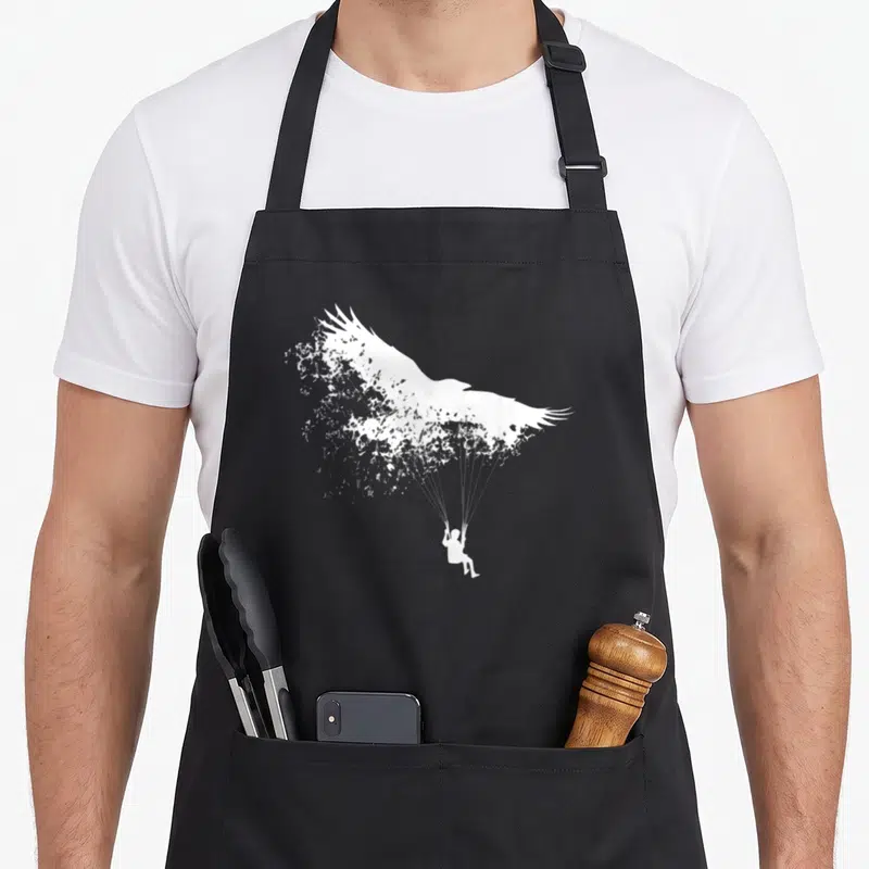 Tablier de cuisine noir avec silhouette blanche d'un sauteur suspendu à une voile d'oiseau stylisée.