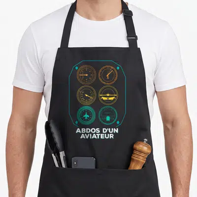 Tablier de cuisine noir avec un tableau de bord avion et le texte Abdos d'un aviateur en blanc et jaune.