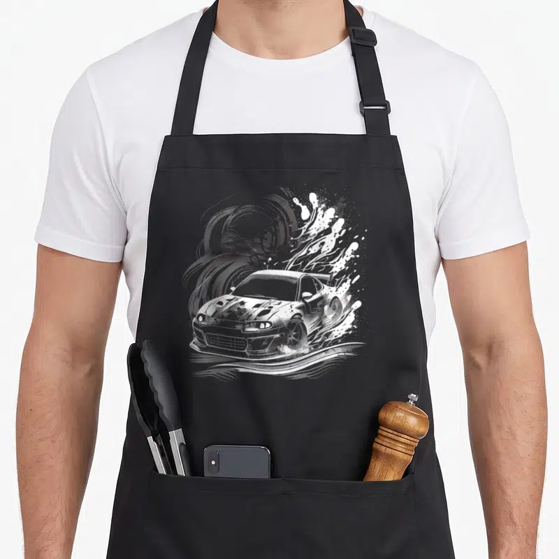 Tablier de cuisine noir avec illustration blanche d'une voiture de sport effectuant une manœuvre de drift dynamique.