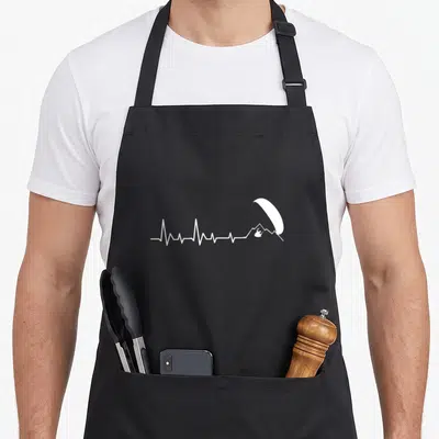 Tablier de cuisine noir avec un motif blanc représentant une ligne de rythme cardiaque se terminant par un parapente au-dessus d'une montagne.