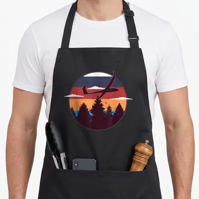 Tablier de cuisine noir avec un cercle illustrant un planeur RC devant un drapeau et des arbres.