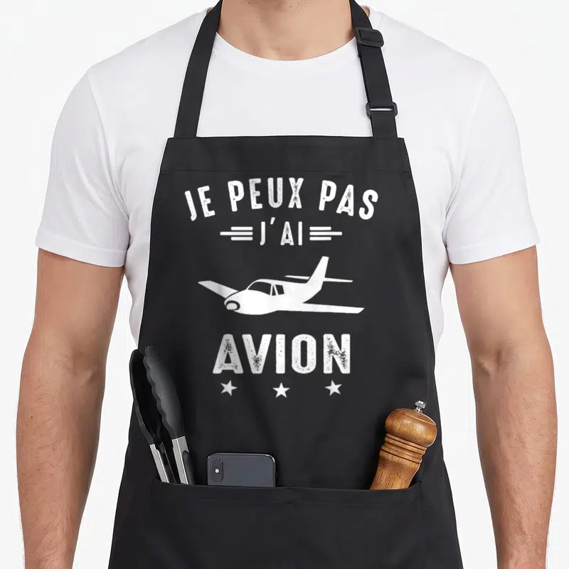 Tablier de cuisine noir avec l'inscription Je peux pas j'ai avion et une silhouette d'avion blanc.