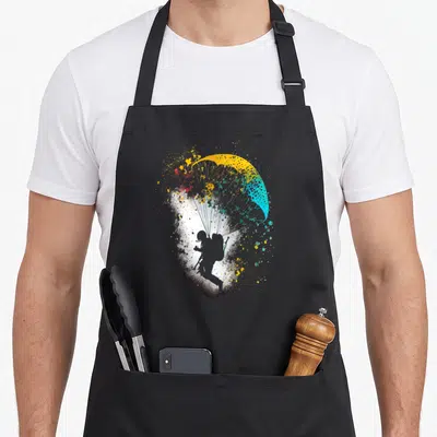 Tablier de cuisine noir avec silhouette de parachutiste et voile jaune turquoise aux éclaboussures artistiques.