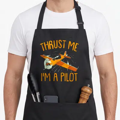 Tablier de cuisine noir avec illustration d'avion orange et texte Thrust Me I'm A Pilot en lettres capitales.