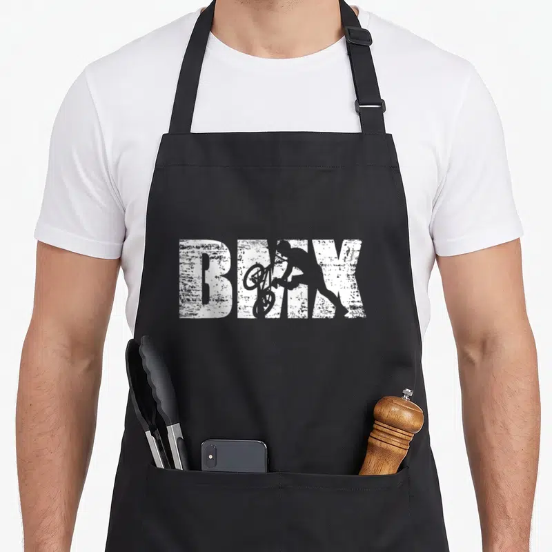 Tablier de cuisine noir avec inscription BMX et silhouette d'un cycliste effectuant un saut acrobatique en blanc.