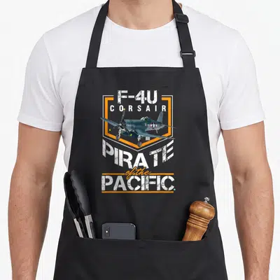 Tablier de cuisine noir avec illustration d'avion F-4U Corsair et texte Pirate of the Pacific en blanc et orange.