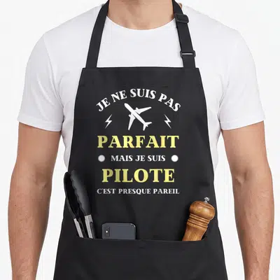 Tablier de cuisine noir avec un avion blanc et le texte Je ne suis pas parfait mais je suis pilote en jaune et blanc.