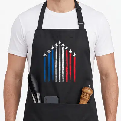 Tablier de cuisine noir avec neuf silhouettes d'avions traçant des fumées bleue blanche et rouge en formation architecturale.