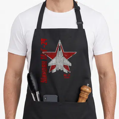 Tablier de cuisine noir avec illustration technique d'un MiG-29 sur étoile rouge et texte cyrillique vertical.