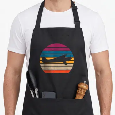 Tablier de cuisine noir avec silhouette avion volant sur cercle rayé rose bleu orange beige et rouge style rétro