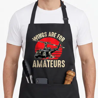 Tablier de cuisine noir avec illustration d'hélicoptère et texte « Wings are for amateurs » sur fond rouge circulaire.
