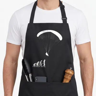 Tablier de cuisine noir avec illustration blanche montrant l'évolution humaine se terminant par un parapentiste en vol.