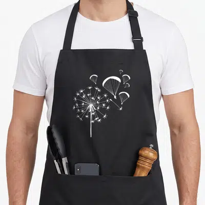 Tablier de cuisine noir avec illustration blanche d'un dandelion dont les graines deviennent des parachutes de parapente.