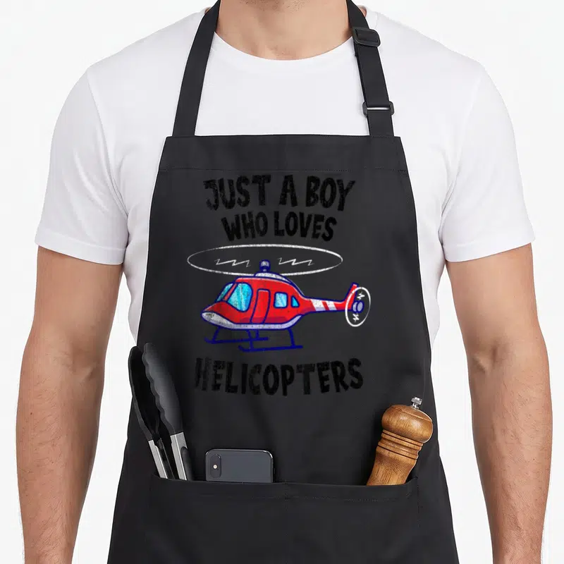 Tablier de cuisine noir avec hélicoptère rouge et texte Just a boy who loves helicopters en lettres noires.