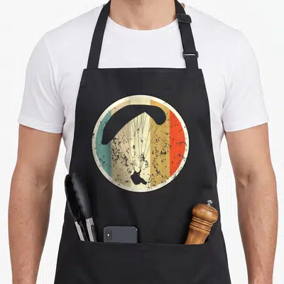 Tablier de cuisine noir avec un parapente vintage sur fond de bandes colorées circulaires